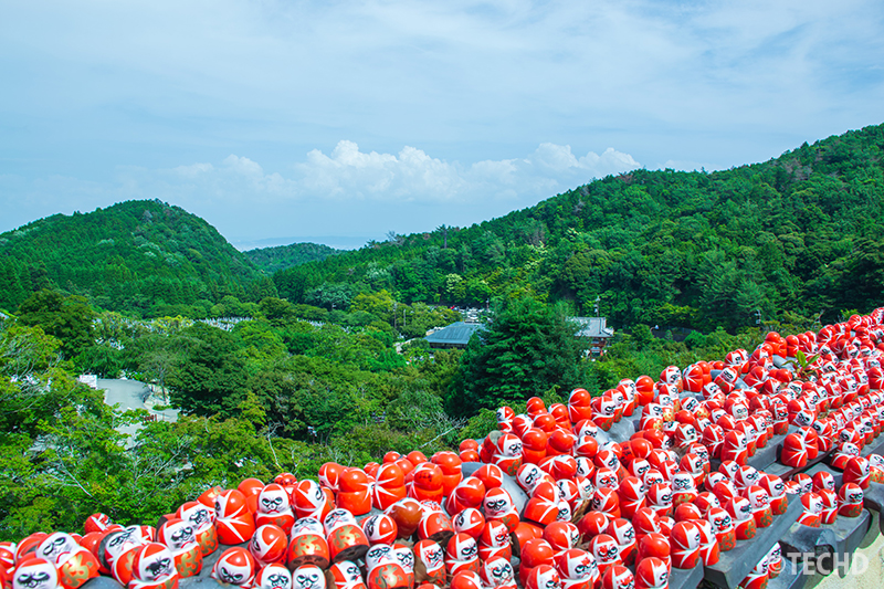 瓦にたくさんの勝ちダルマと上から見た勝尾寺の風景