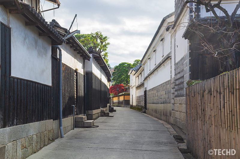 倉敷美観地区の裏通りにある白壁と黒塀の街並み。人通りの少ない静かな路地が奥へと続いている風景