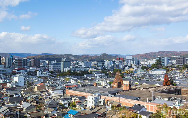 倉敷市の高台から見下ろした市街地の俯瞰風景。美観地区の街並みとレンガ造りの建物、遠方に広がるビル群と山並みが写る