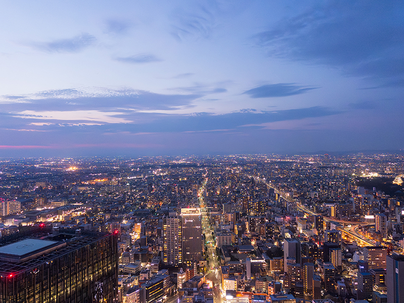スカイプロムナードから見た北方向の夜景。夕暮れ空の下に広がる名古屋の街並みと、点灯し始めた建物や道路の灯りが印象的。