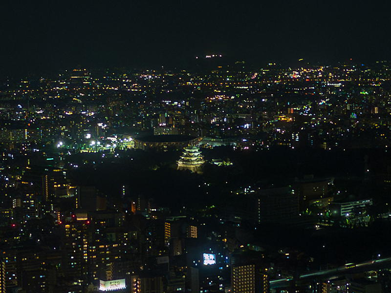 スカイプロムナードから望遠レンズで撮影した名古屋城の夜景。ライトアップされた城が市街地の中にくっきりと浮かび上がっている。