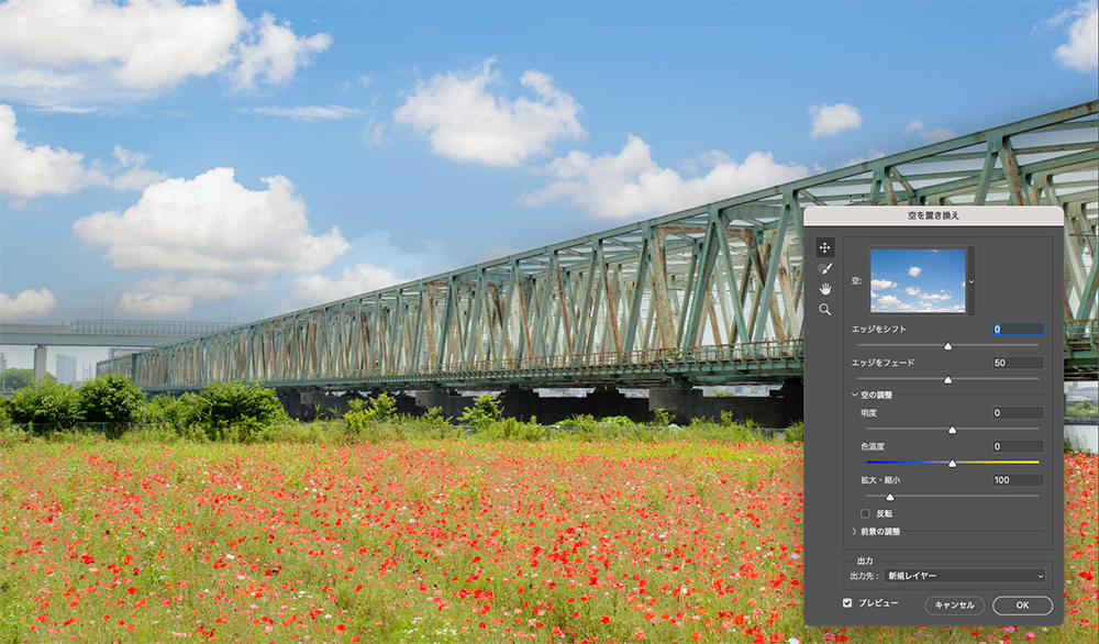 Photoshopで鉄橋と赤い花畑の写真を加工し、空を鮮やかな青空と白い雲に置き換えた様子。不要物も削除され、右側には「空を置き換え」パネルが表示されている。