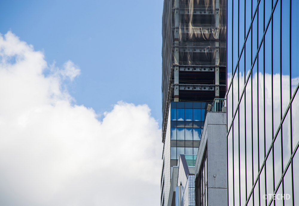 ガラス面に雲が映り込む高層ビル。手前のビルの反射にピントが合い、奥の建設中ビルがややソフトフォーカス気味。Adobe Stockの審査で「品質の問題」として却下された写真。