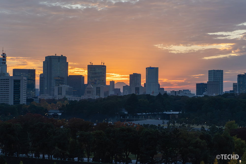 新丸ビルの7階から撮影した夕景。高層ビル群の向こうに、夕日に照らされた富士山のシルエットが浮かび上がる。