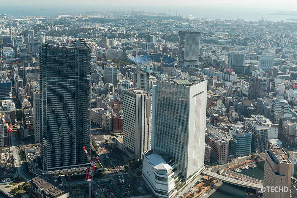 横浜ランドマークタワーから望む横浜スタジアム方面の遠景。青い屋根が印象的なスタジアムと街並みが広がる昼景。