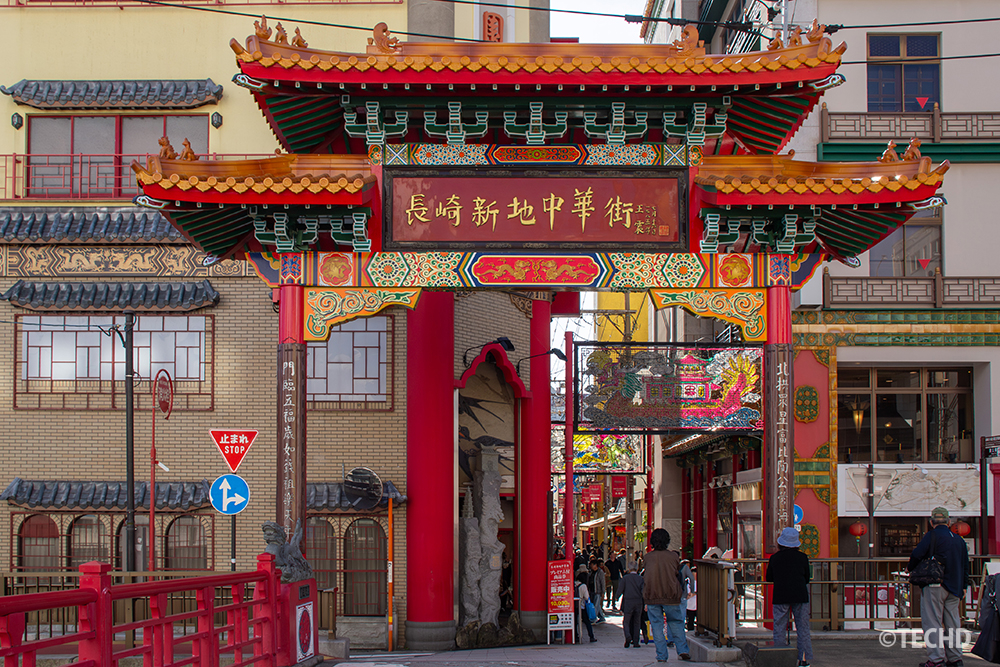 長崎新地中華街の朱色の牌楼と周囲の建物、行き交う人々のにぎわい。