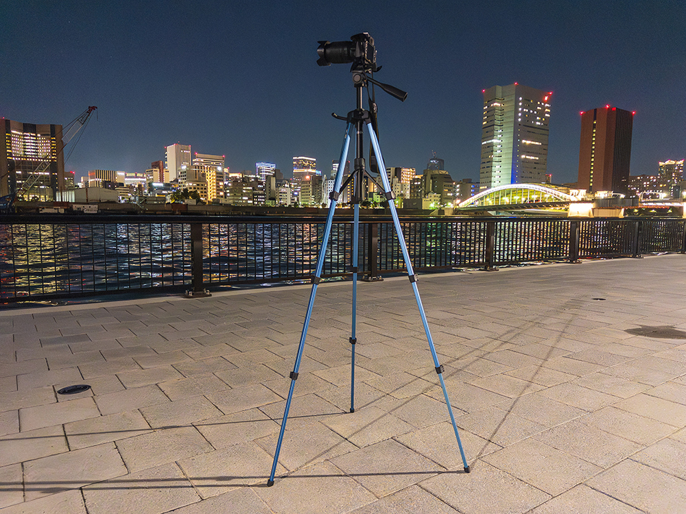 SLIK GX-S 6400にNIKON D3100を装着し、夜の街並みを背景に夜景撮影を行っている様子