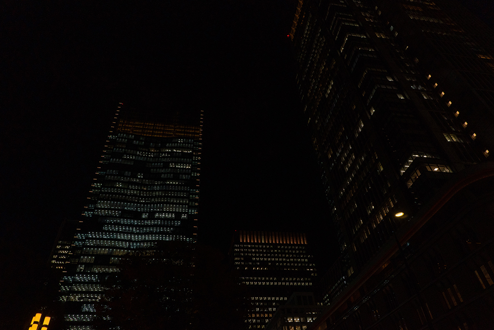 東京駅丸の内駅前広場で、夜の高層ビル群をISO800で手持ち撮影した写真。建物の明かりは控えめで、全体的に暗めの露出になっている。