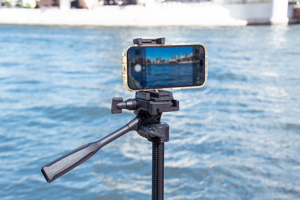 SLIK GX-S 6400にiPhoneを装着し、水辺で撮影している様子。スマホホルダーを使用して安定した構図で撮影しているシーン