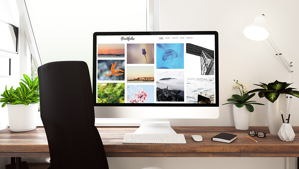 デスクに置かれたデスクトップパソコンの画面に、グリッド状に美しく整列された写真ポートフォリオが表示されている様子。ブログやPinterestでジャンル別ギャラリーを作成した際の完成イメージ。
