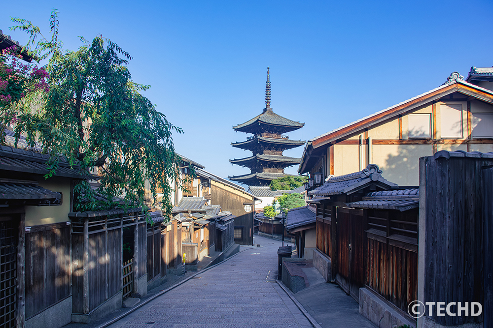 京都・東山エリアにある八坂の塔（法観寺）と、それへと続く伝統的な家並みの風景。石畳の通りと快晴の青空が広がる風景写真。