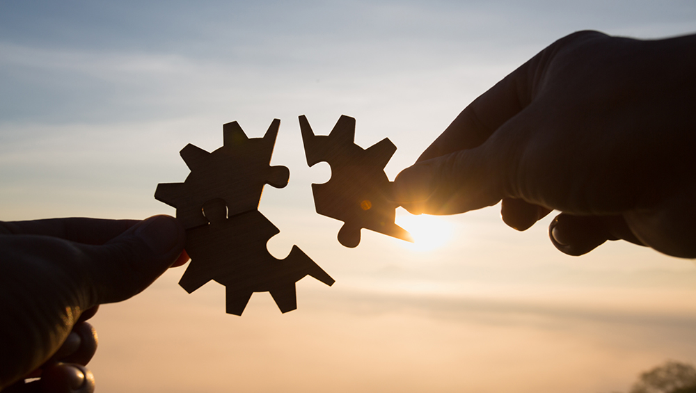 朝焼けを背景に、歯車の形をしたパズルピースを組み合わせる手。ブログとPinterestが連携し、一つの大きな導線として機能し始めるイメージ。