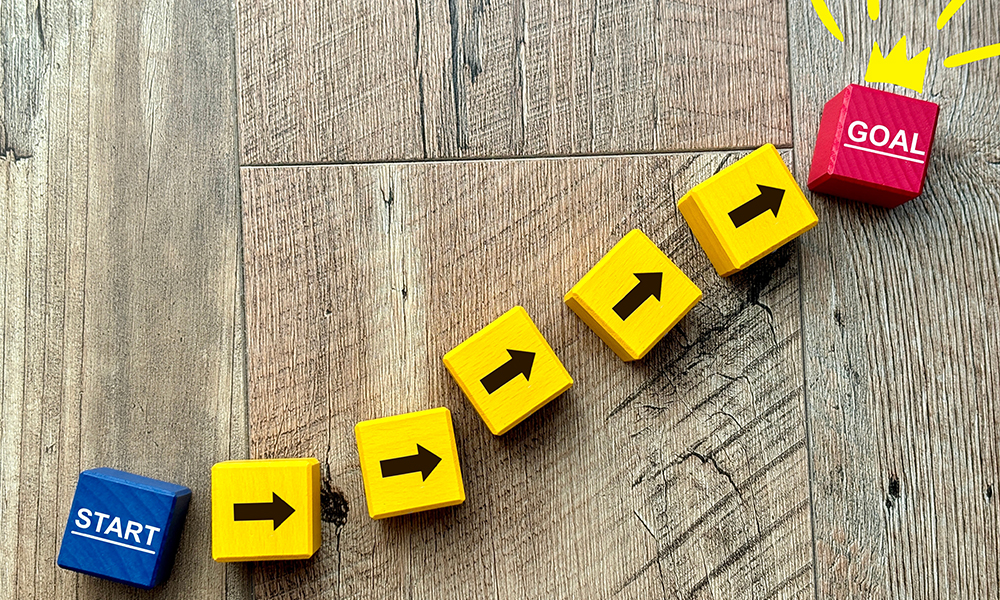 木目調の床に並べられた、「START」から「GOAL」へと続く矢印のブロック。ストックフォトで資産を構築し、目標収益を達成するまでのロードマップをイメージした画像。