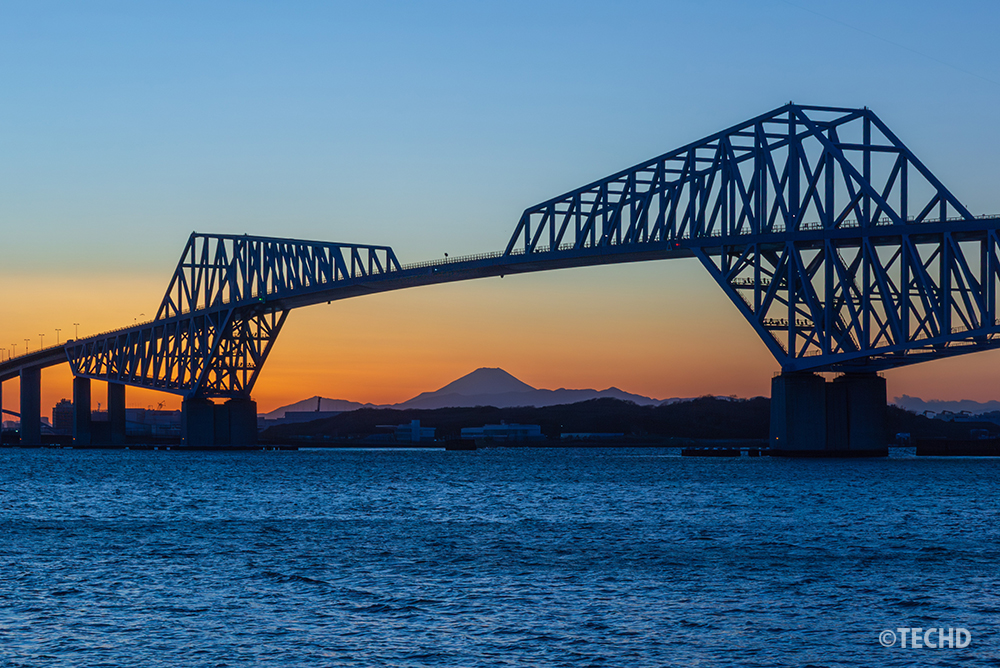 日没後のマジックアワー。地平線が鮮やかなオレンジに染まり、富士山の稜線が際立つ。東京ゲートブリッジのライトアップが始まる直前の静寂。