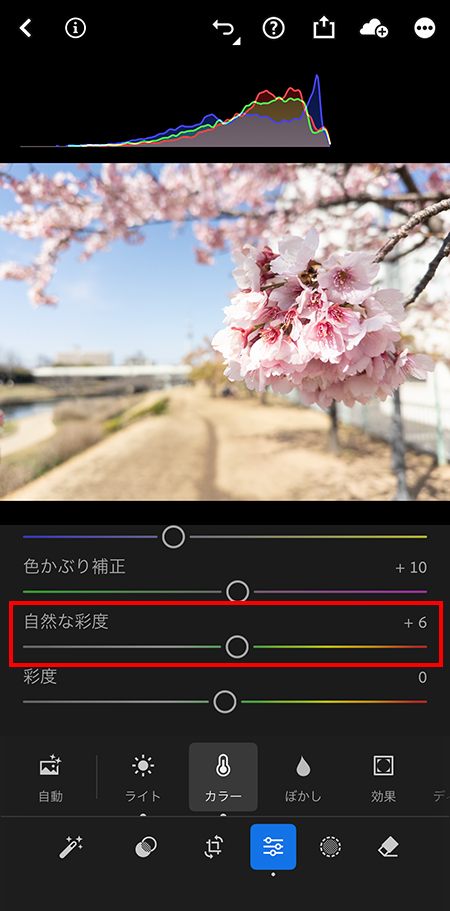 スマホ版Lightroomで「自然な彩度」を調整中の画面。空の青や桜のピンクを不自然にならない程度に鮮やかに補正している様子。